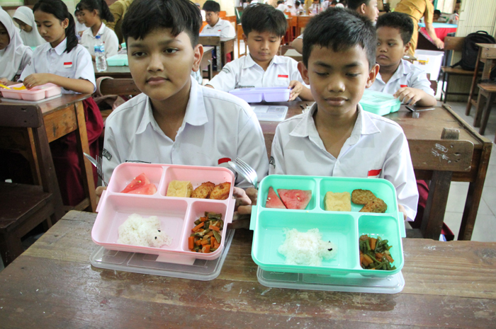 KOMPOSISI MENU: Siswa menunjukkan menu makan bergizi gratis (MBG).