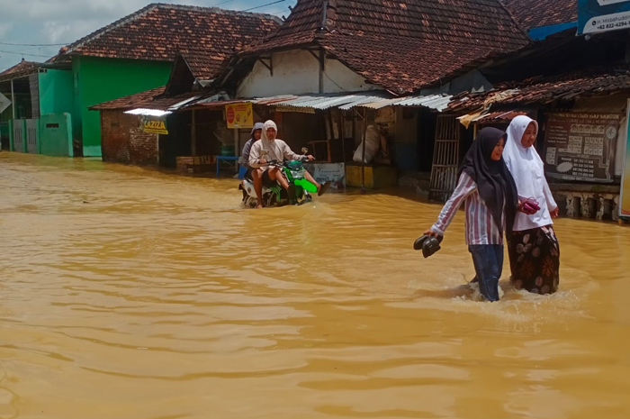 TAK KUNJUNG SURUT: Sejumlah warga Kecamatan Mejobo menerjang banjir di Perempatan Mejobo kemarin.