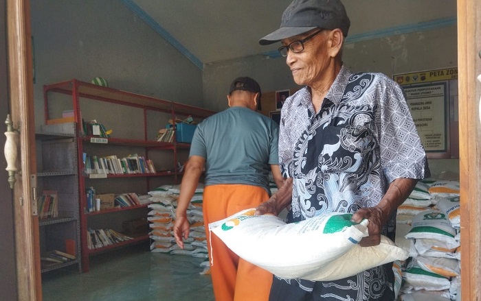 DIBANTU: Salah satu penerima bantuan mengambil beras di kantor balai Desa/Kecamatan Margorejo belum lama ini.
