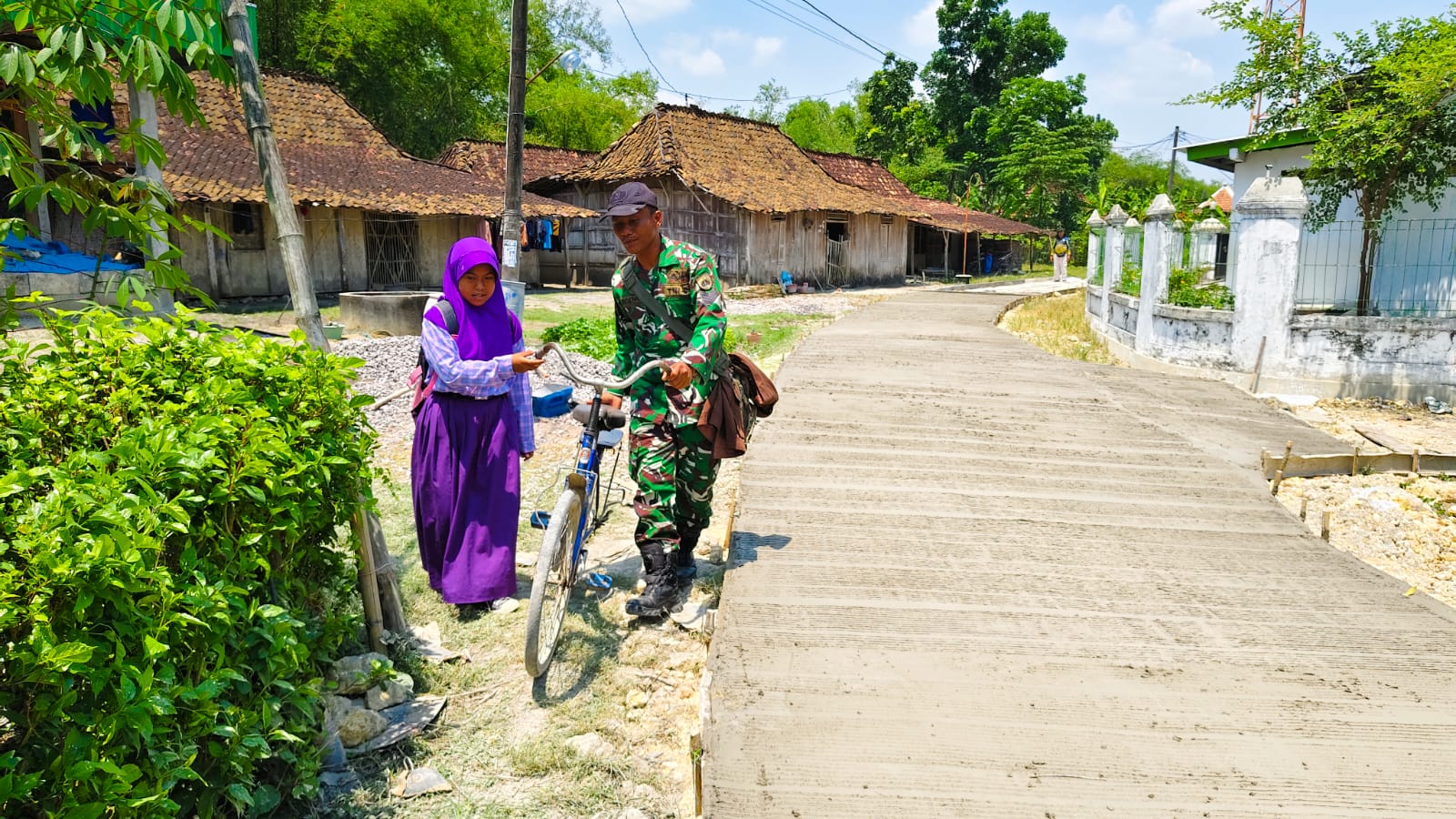 PEDULI: Satgas TMMD ke-126 Reguler saat membantu pelajar melintas di jalan rabat beton yang sedang proses pengerjaan.
