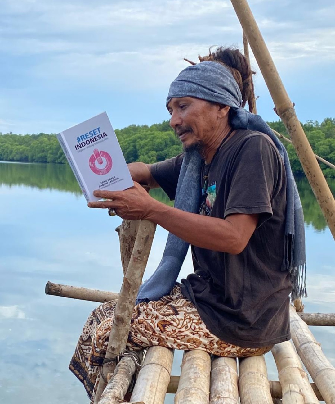 TEKUN: Bambang Zakaria tengah bersantai sembari membaca buku di pelataran kediamannya di Desa Kemujan.