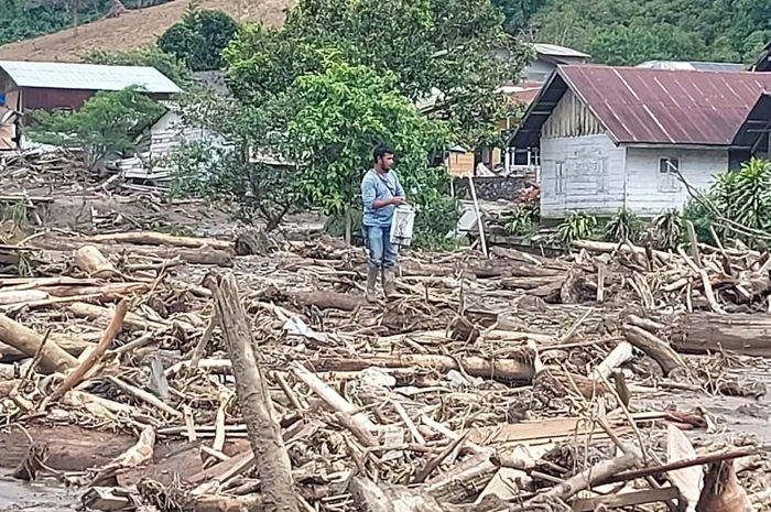 Warga Takengon berdiri di antara kayu-kayu yang terbawa banjir dan longsor.