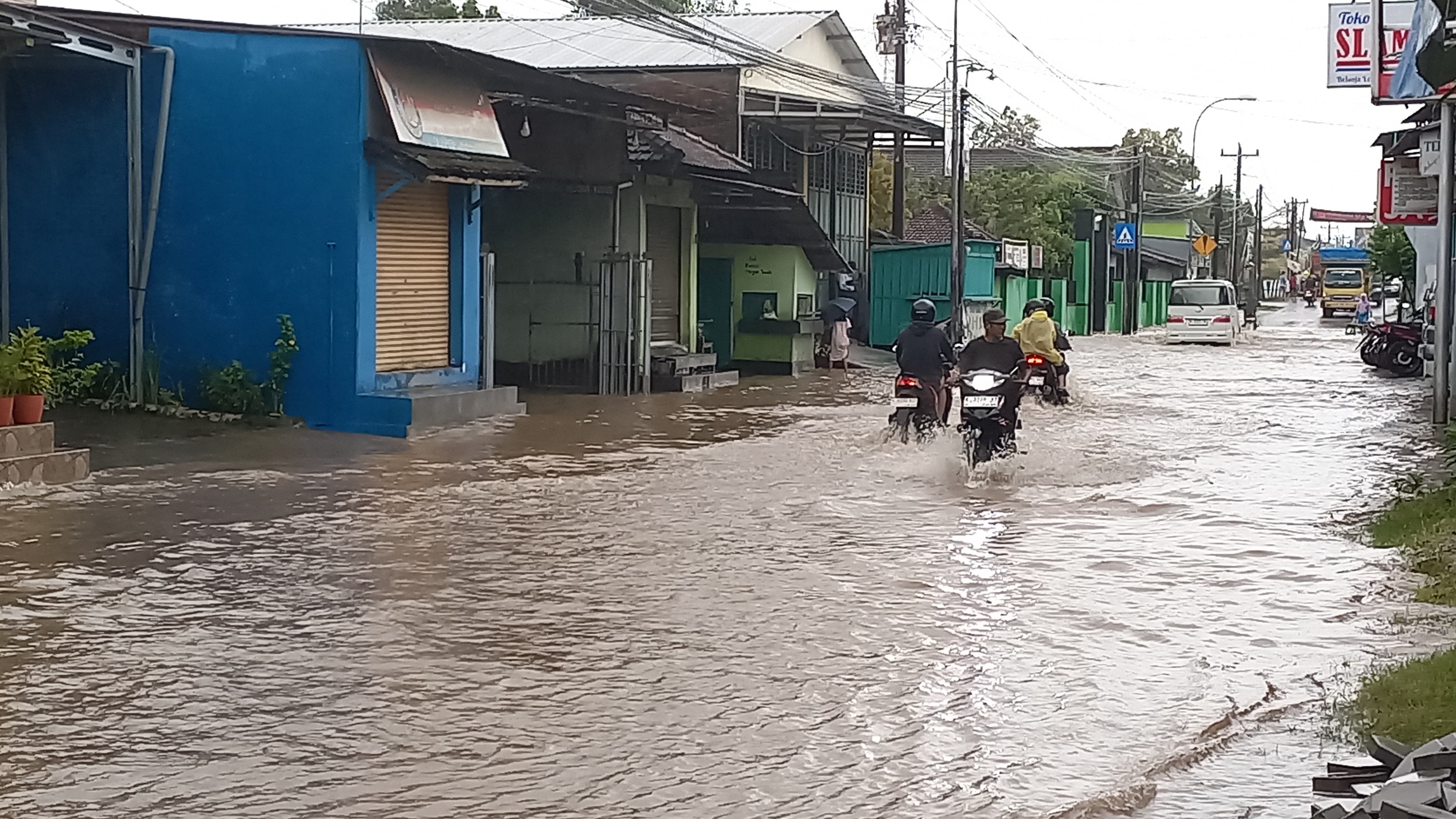 HATI-HATI: Warga melintasi jalan Alternatif Kudus-Pati di Desa Mejobo yang terendam banjir.