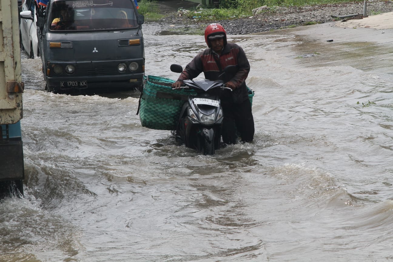 MENERJANG: Penggendara sepeda motor mendorong motornya yang mogok usai menerjang banjir di Jalan Kudus-Purwodadi.