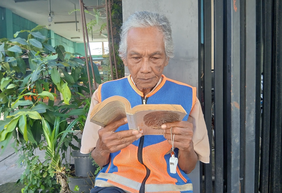SEMANGAT: Suyono, 78 saat membaca di tengah aktivitas sebagai tukang parkir.