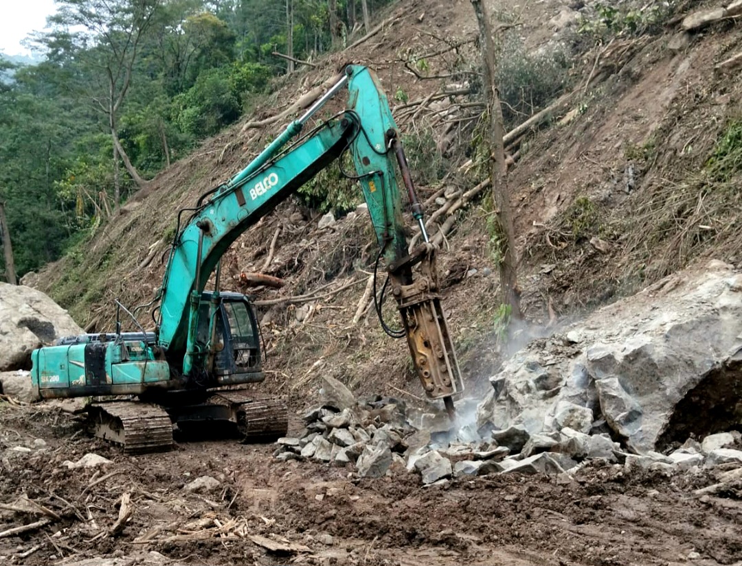 BERTAHAP: Operator alat berat tengah berupaya memecahkan batu di badan jalan yang menuju Desa Tempur pada Jumat (13/2).