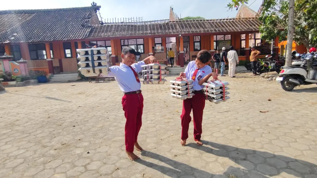 SAMBUT GEMBIRA – Siswa SD N Tanggirejo membawa Makan Bergizi Gratis (MBG) dengan penuh ceria meski ruang kelas mereka roboh dan harus belajar berdesakan di Musolla, Senin (27/7). 