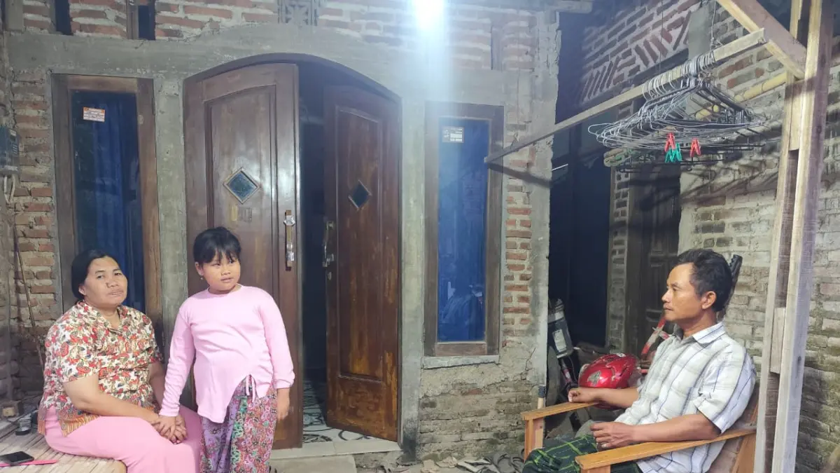 RUMAH KECIL: Atminah bersama anaknya (kiri) bersama Sholikin suaminya saat duduk di depan rumah. (INDAH SUSANTI/RADAR KUDUS)