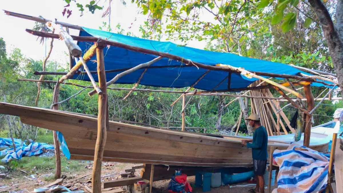 DETAIL: Pengrajin kapal kayu di Pulau Rengit, Kabupaten Belitung, Kepulauan Bangka Belitung, Itam Ali, saat menyelesaikan pembuatan kapal. Kehadiran layanan listrik 24 jam melalui PLTS Rengit memungkinkannya memanfaatkan peralatan listrik kapan pun, sehingga mendukung produktivitas pekerjaannya.