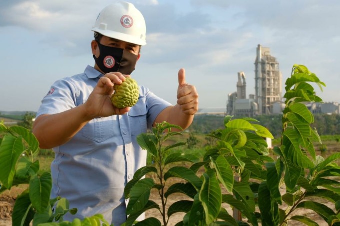 PEDULI: Karyawan Semen Gresik menunjukkan hasil panen buah srikaya dengan latar Pabrik Semen Gresik di Rembang, Jawa Tengah, Rabu (30/12). (PT SG FOR RADAR KUDUS)
