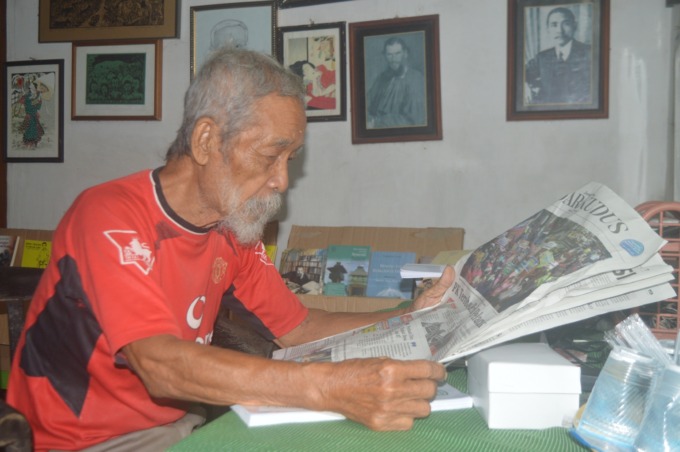 BERSANTAI: Soesilo Toer membaca koran Jawa Pos Radar Kudus edisi kemarin.  (Subekan/Radar Kudus)