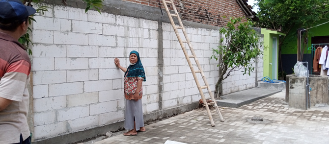 MERATAPI: Sutikah menunjukkan jalan ke rumahnya di RT 8/RW II, Desa/Kecamatan Mejobo, Kudus, yang ditutup tembok setinggi 2,5 meter. (EKO SANTOSO/RADAR KUDUS)