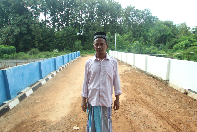 PANUTAN: Kholilullah Al-Ibrahim, berdiri dengan latar belakang jembatan yang dibangun menggunakan anggaran pribadi. (MOH. NUR SYAHRI MUHARROM/ RADAR KUDUS)