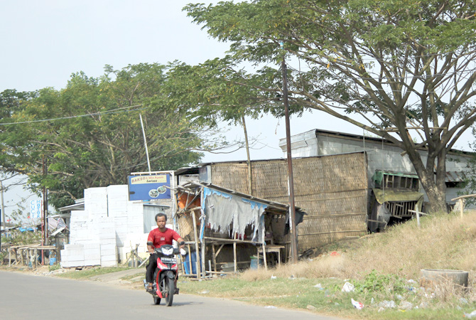 TAK BERIZIN: Pengendara melintas di samping deretan bangunan yang berdiri di atas tanggul Sungai Serang Desa Kedungmalang, Kedung, kemarin. (MOH. NUR SYAHRI MUHARROM/RADAR KUDUS)