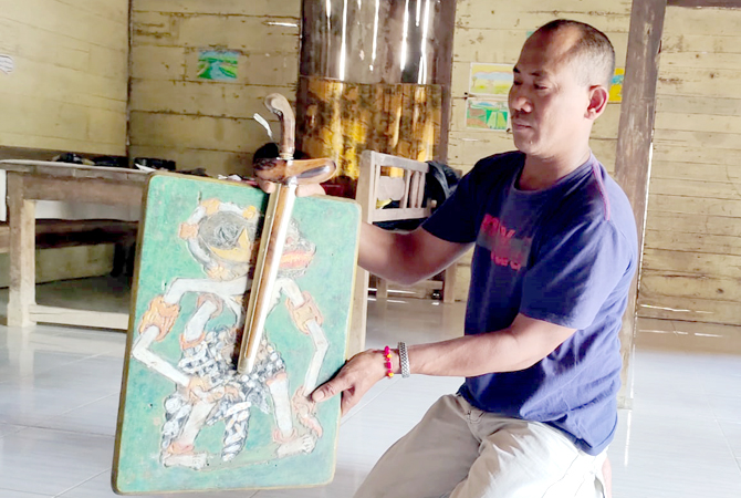 BERI CONTOH: Sagik memperlihatkan cara memajang keris di dinding yang diberi semacam lukisan gambar wayang berbahan kayu di rumahnya. (ZAIMUL CHAMIM/RADAR KUDUS)
