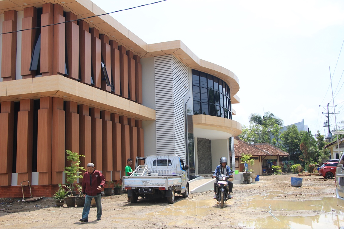MASIH BECEK: Sejumlah pegawai melintas di halaman Kantor Dindikpora Rembang yang becek selepas diguyur hujan kemarin (2/1/2024). (WISNU AJI/RADAR KUDUS)