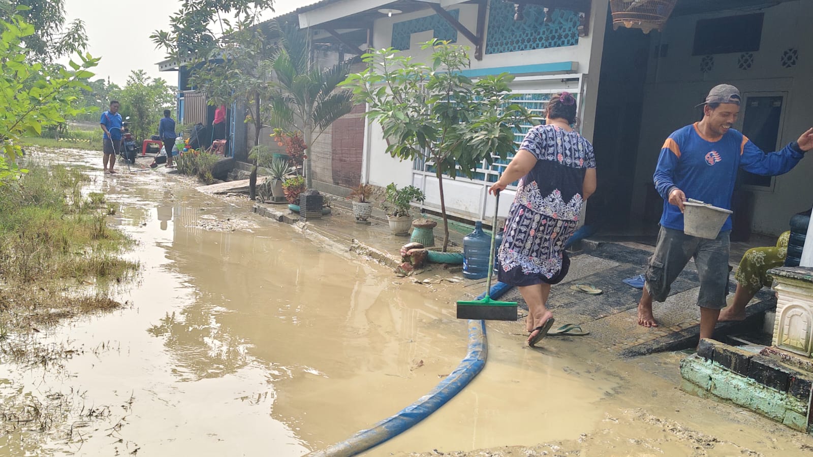 BERSIHKAN LUMPUR: Warga Perumahan Permata Hijau Kalongan, Purwodadi membersihkan rumah usai banjir bandang, Minggu dini hari (24/11). (SIROJUL MUNIR/RADAR KUDUS)