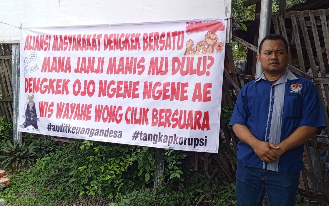 DILIHATKAN: Salah satu warga menunjukkan baner unjukvrasa di depan Balai Desa Dengkek, Pati belum lama ini.