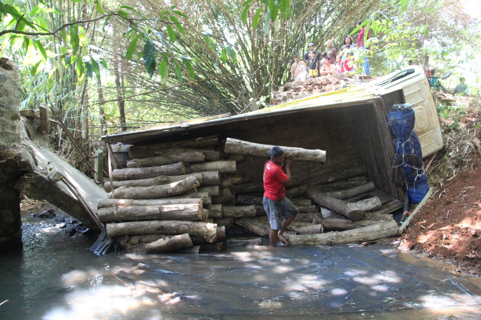 EVAKUASI: Warga bantu melangsir muatan kayu balok dari atas bak truk yang terguling ke sungai.