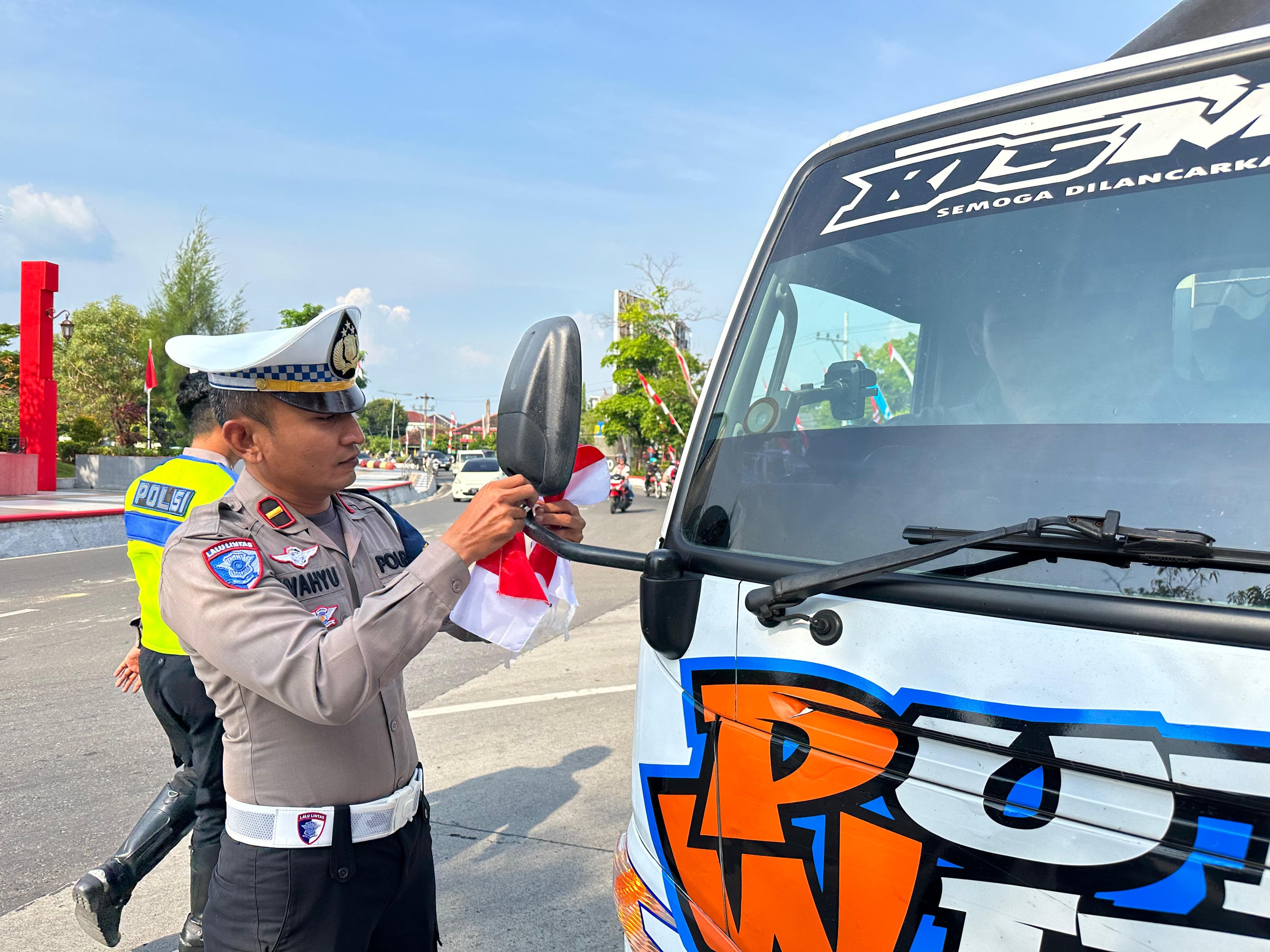 NASIONALISME: Satlantas Polres Grobogan memasangkan bendera merah putih ke truk yang melintas di kawasan perkotaan Purwodadi.