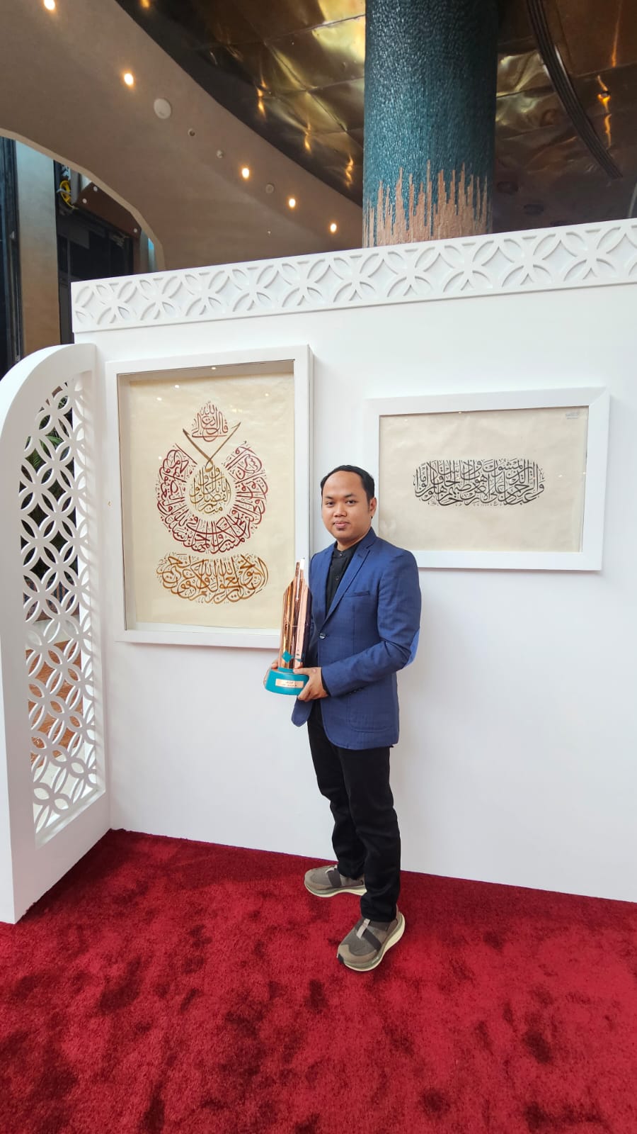 KELAS DUNIA: Huda Purnawadi membawa trofi di depan dua karya kaligrafinya yang memenangi lomba kaligrafi internasional &rdquo;Al-Akhlaq Award&rdquo; di Doha, Qatar.(DOK PRIBADI UNTUK RADAR PATI)