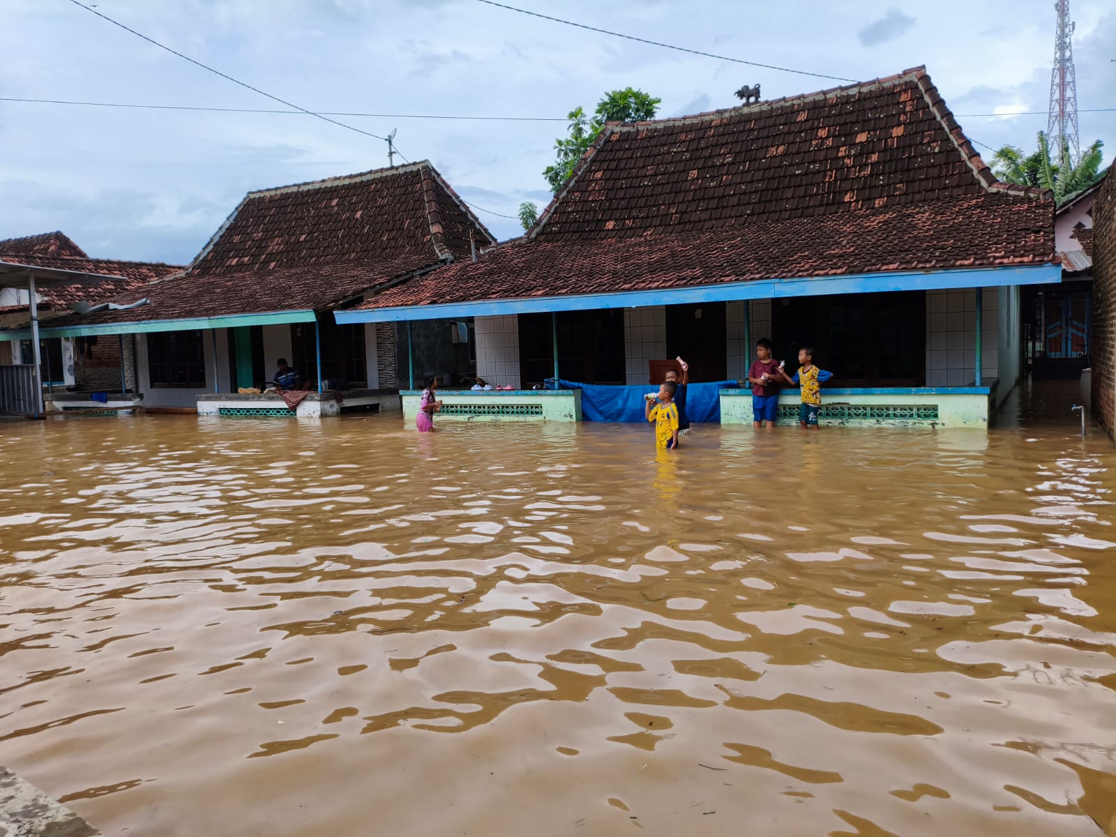 Anak - anak sedang bermain di depan rumah yang terendam banjir di Desa Widorokandang Pati Kota. (ACHMAD ULIL ALBAB/RADAR KUDUS)
