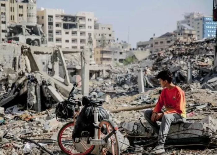 Seorang pemuda Palestina duduk di samping sepedanya di tengah puing-puing bangunan yang hancur di Kota Gaza di jalur Gaza utara setelah  pemboman Israel