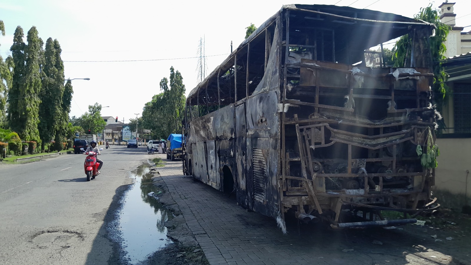 HANGUS TERBAKAR: Pengendara sepeda motor melintas di sekitar bangkai bus Pahala Kencana di Polres Bangkalan, Senin (2/6). (M. KHOLIL RAMLI/JPRM)