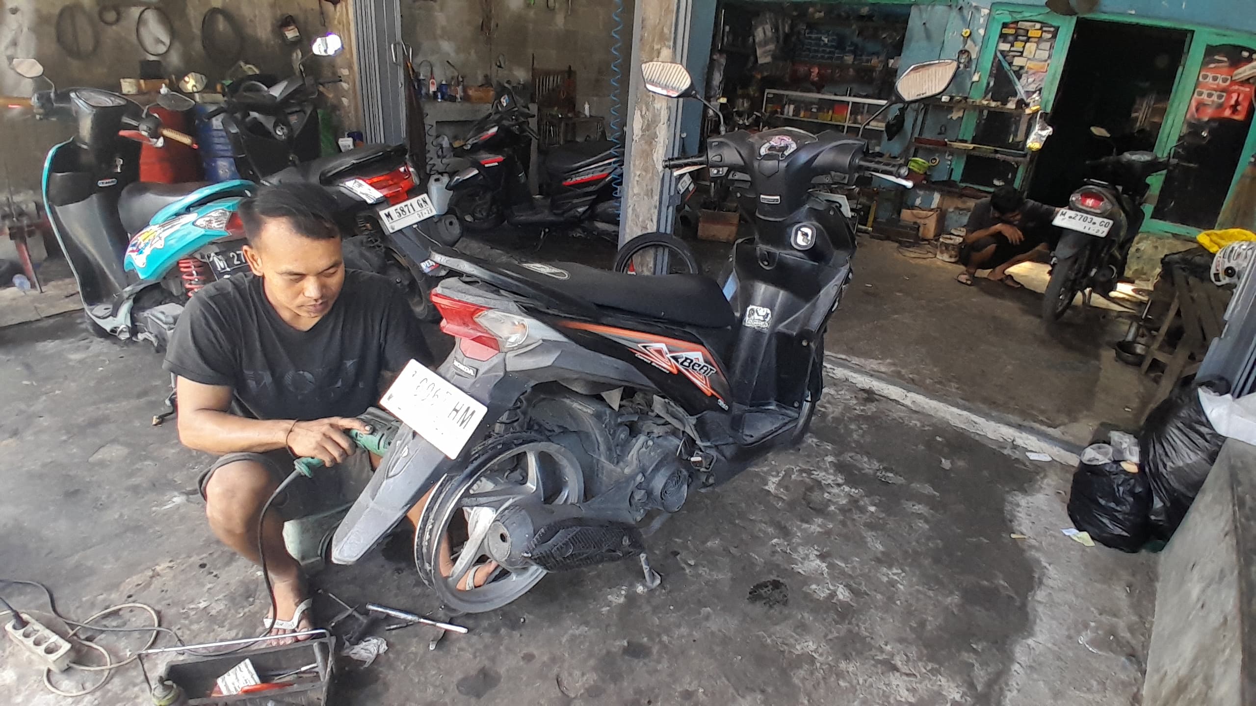 KERJA KERAS: Mawes, mekanik di salah satu bengkel otomotif  di Jalan RE Martadinata, Bangkalan, sedang memperbaiki sepeda motor warga, Kamis (12/6). (M. KHOLIL RAMLI/JPRM)