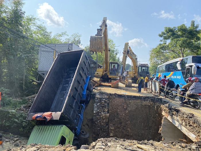 DIEVAKUASI: Truk Fuso yang terperosok ke sungai di area proyek Jembatan Pangeleyan, Kecamatan Tanah Merah, Bangkalan, dievakuasi petugas dengan ekskavator. (ROSATIN NUR/JPRM)