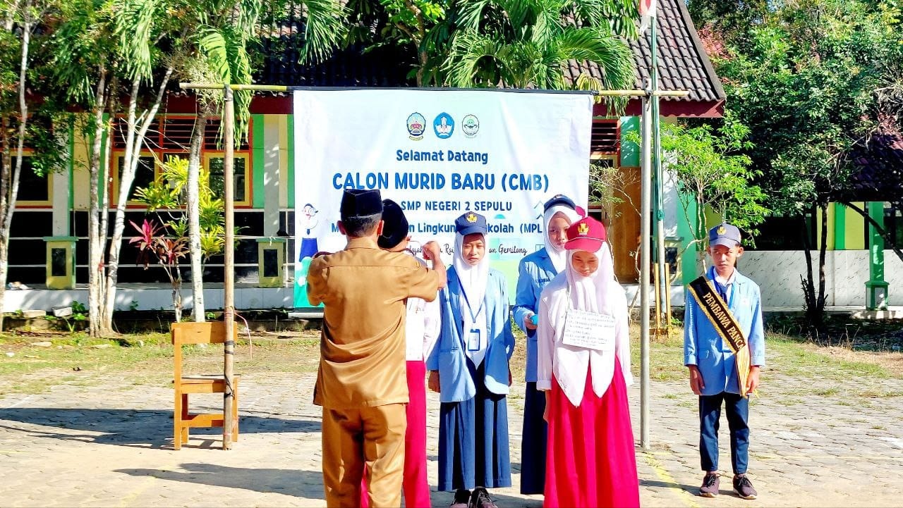 PEMBUKAAN: Kepala UPTD SMPN 2 Sepulu Sunarto memasang tanda peserta MPLS, Selasa (17/7)
