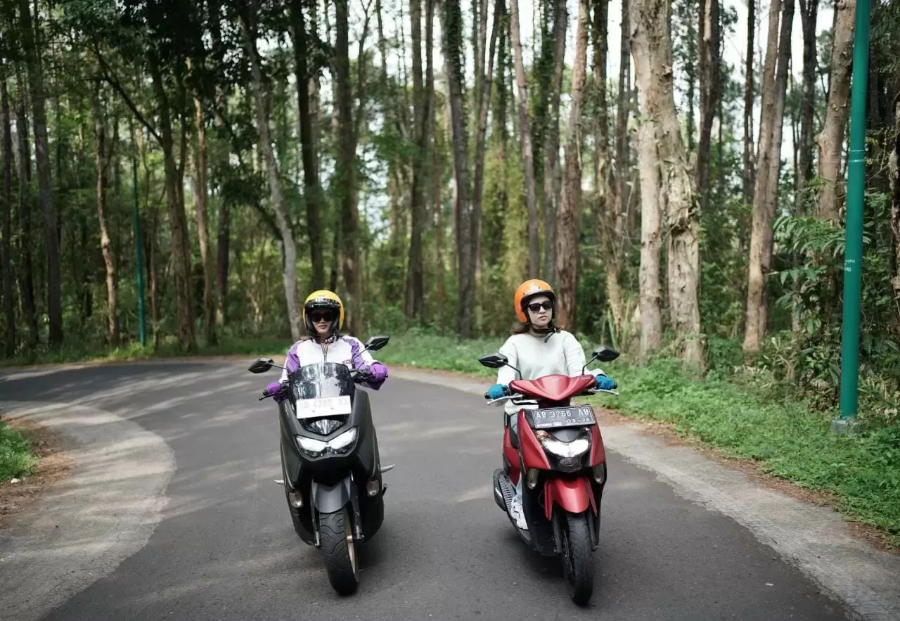 Ilustrasi dua perempuan sedang mengendarai sepeda motor matic di tanjakan