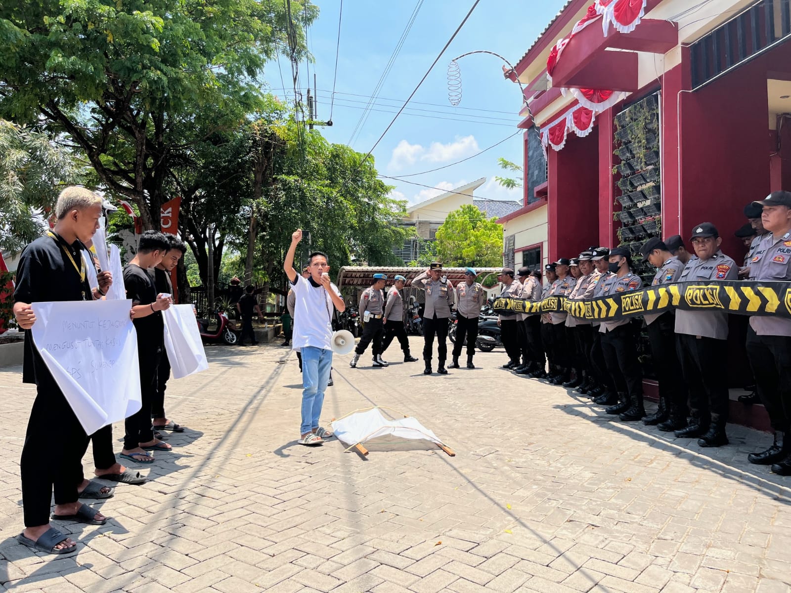 DIJAGA KETAT: Gerakan Pemuda Madura (GPM) dan Komunitas Laknat Koruptor (KLK) melakukan aksi terkait korupsi BSPS di depan kantor Disperkimhub Sumenep.&nbsp;