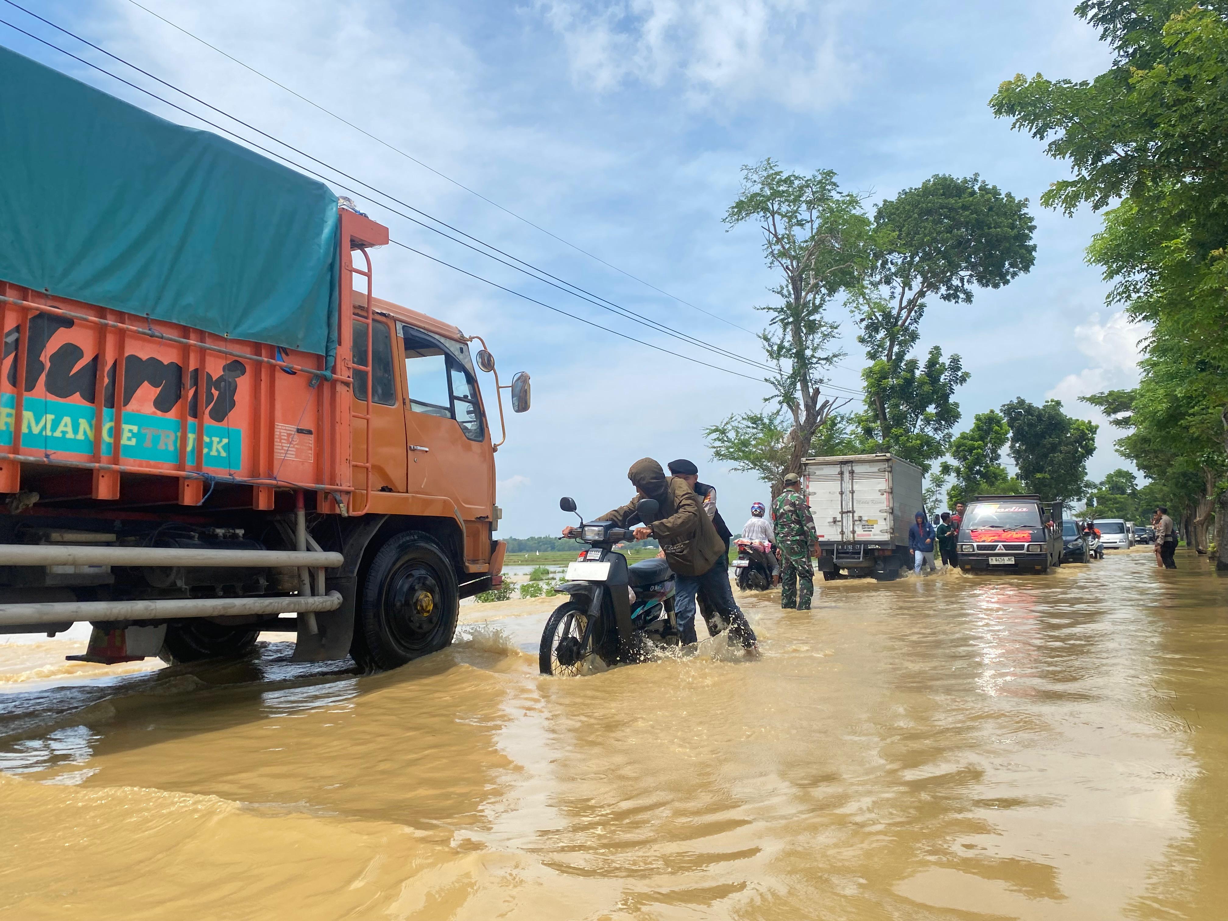 MELUAP: Petugas Polri membatu pengendara motor melintas karena terjebak banjir di Jalan Raya Jrengik, Sampang, pada Rabu (19/11).&nbsp;  &nbsp;