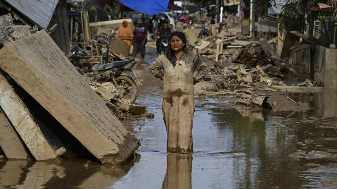 Foto menunjukkan seorang perempuan berlumuran lumpur berdiri di jalanan berlumpur setelah banjir di Aceh Tamiang pada 6 Desember 2025. (YT HARIONO/AFP)
