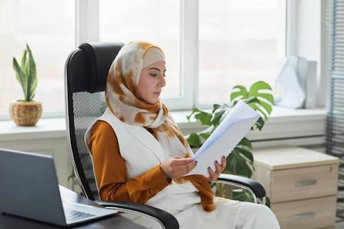 Seorang perempuan membaca lembaran dokumen di ruangannya.