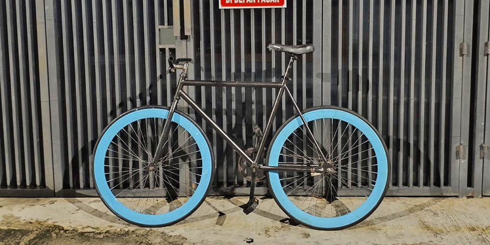Sebuah sepeda fixie dengan velg biru mencolok terparkir di depan pagar&mdash;sebuah potret kebangkitan skena fixie gear di tengah kota.