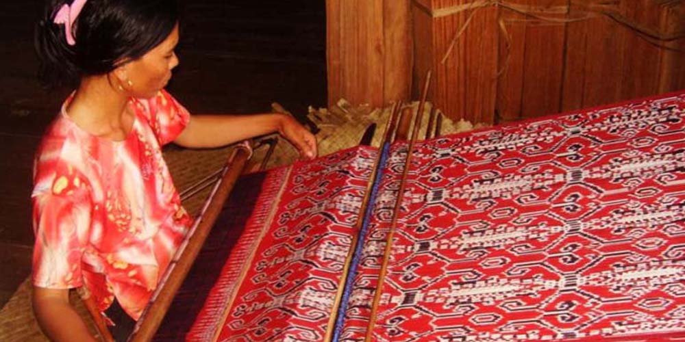 Seorang perempuan Dayak tengah menenun kain tradisional di Kalimantan. Setiap helai benang yang disusun dengan teliti ini menyimpan makna spiritual dan filosofi kehidupan masyarakat adat.