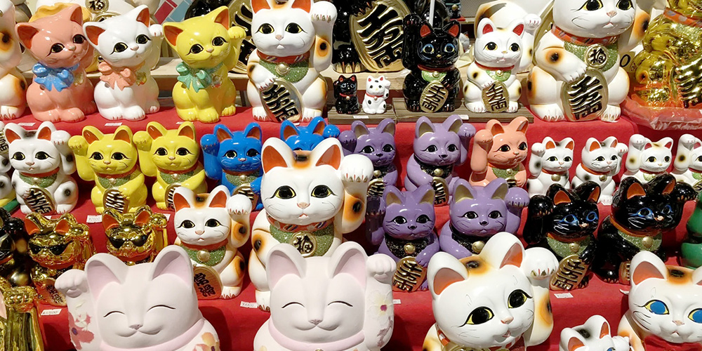 Deretan patung Maneki Neko dengan berbagai warna dan gaya tangan melambai. Setiap warna melambangkan doa berbeda&mdash;dari keberuntungan, rezeki, hingga perlindungan.