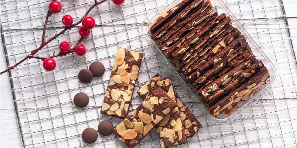 Brownies crispy topping almond tersusun rapi dalam wadah bening, menampilkan lapisan tipis renyah dengan taburan kacang yang membuat tampilannya semakin menggugah selera.