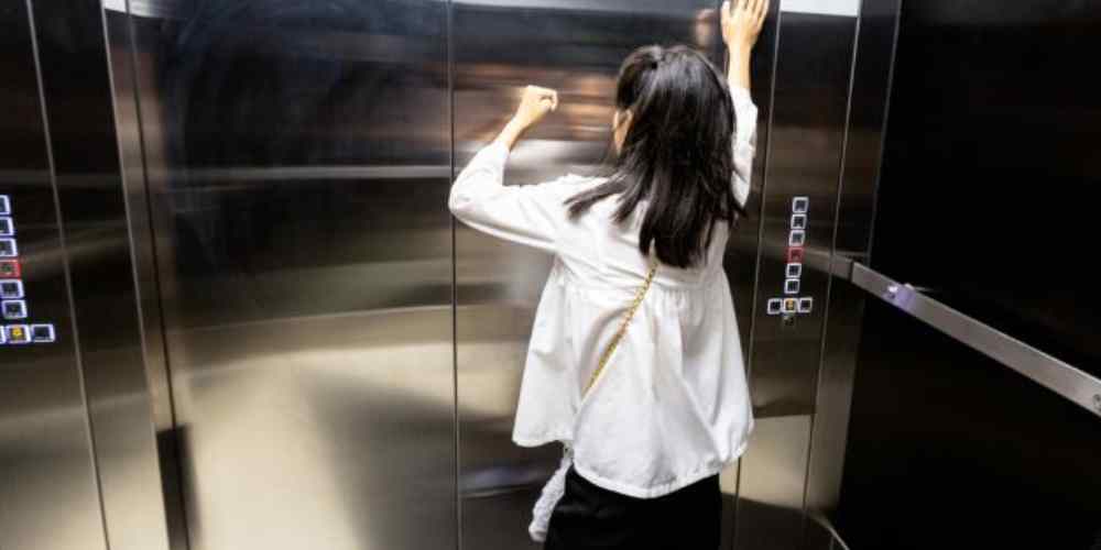 Seorang perempuan tampak panik di dalam lift yang tertutup, menggambarkan gejala klaustrofobia yang bisa muncul tiba-tiba saat berada di ruang sempit atau tanpa jalan keluar.