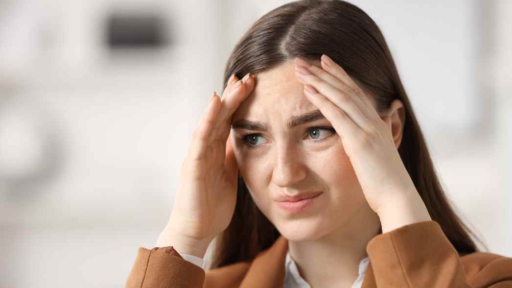 Seorang perempuan memegang kepalanya sambil menunjukkan ekspresi cemas&mdash;gambaran umum gejala social anxiety yang sering muncul tiba-tiba dalam situasi sosial.