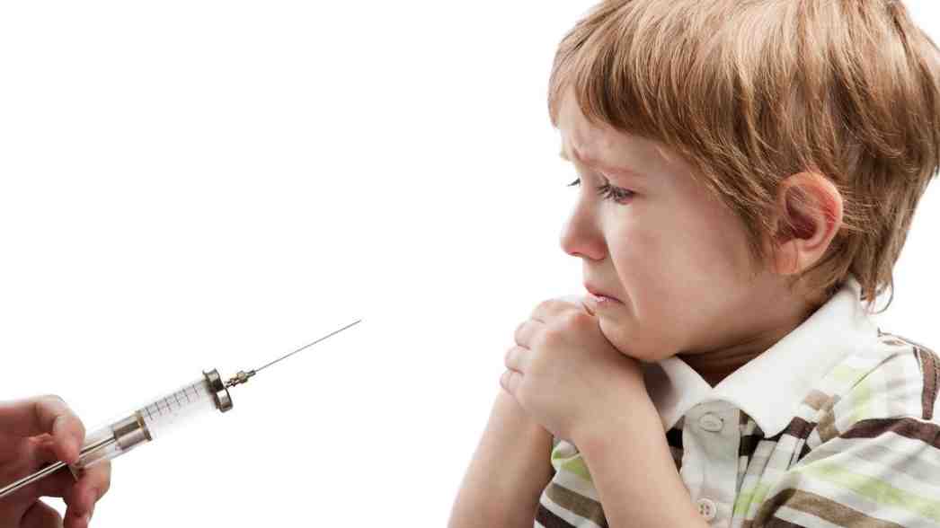 Seorang anak kecil tampak ketakutan dan menangis saat melihat jarum suntik yang diarahkan kepadanya, menggambarkan rasa cemas yang umum terjadi pada anak saat menghadapi prosedur medis.