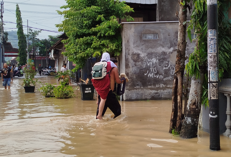 Seorang ayah menggendong anaknya yang masih kelas VI SD untuk mengikuti ujian sekolah di SDN 1 Kelutan yang terdampak banjir