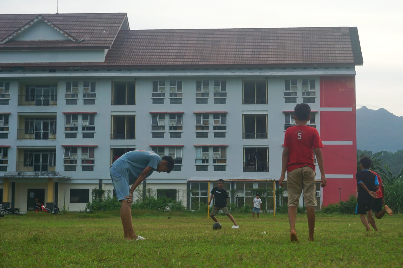Anak-anak kecil asyik bermain bola dengan latar belakang Rusunawa Prigi, Minggu (1/6/2025). (DR PERDANA/RADAR TRENGGALEK)