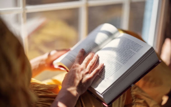 Seseorang menikmati waktu sendirian sambil membaca buku di kamar pada akhir pekan.
