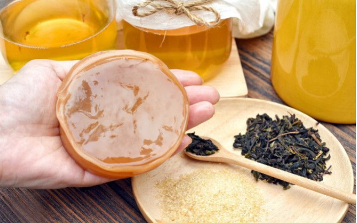 Seseorang memegang Scoby, ada gula dan daun teh serta teh kombucha.
