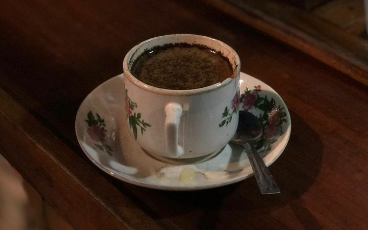 Secangkir kopi hitam tubruk diatas meja kayu yang terlihat menggoda.