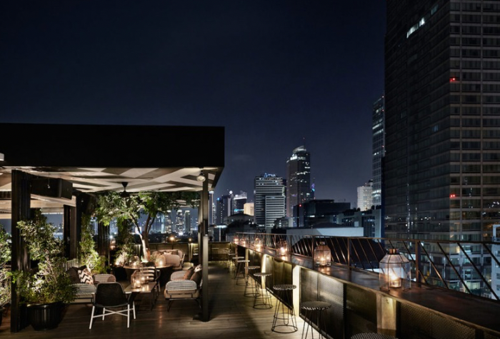 Suasana rooftop hotel di tengah kota yang menampilkan pemandangan gedung-gedung tinggi dan lampu malam yang menawan, menciptakan nuansa tenang dan elegan untuk menikmati staycation.