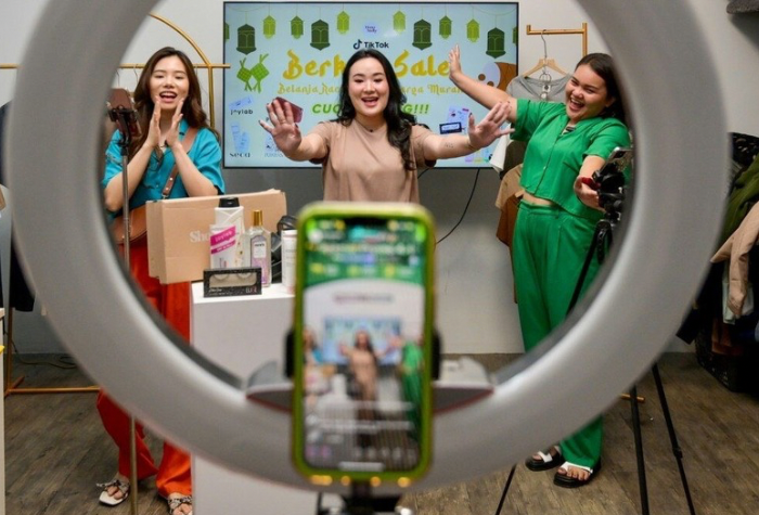 Para kreator konten sedang melakukan siaran langsung di studio mini dengan perlengkapan kamera dan ring light, menampilkan semangat dan kreativitas dalam dunia hiburan digital modern.